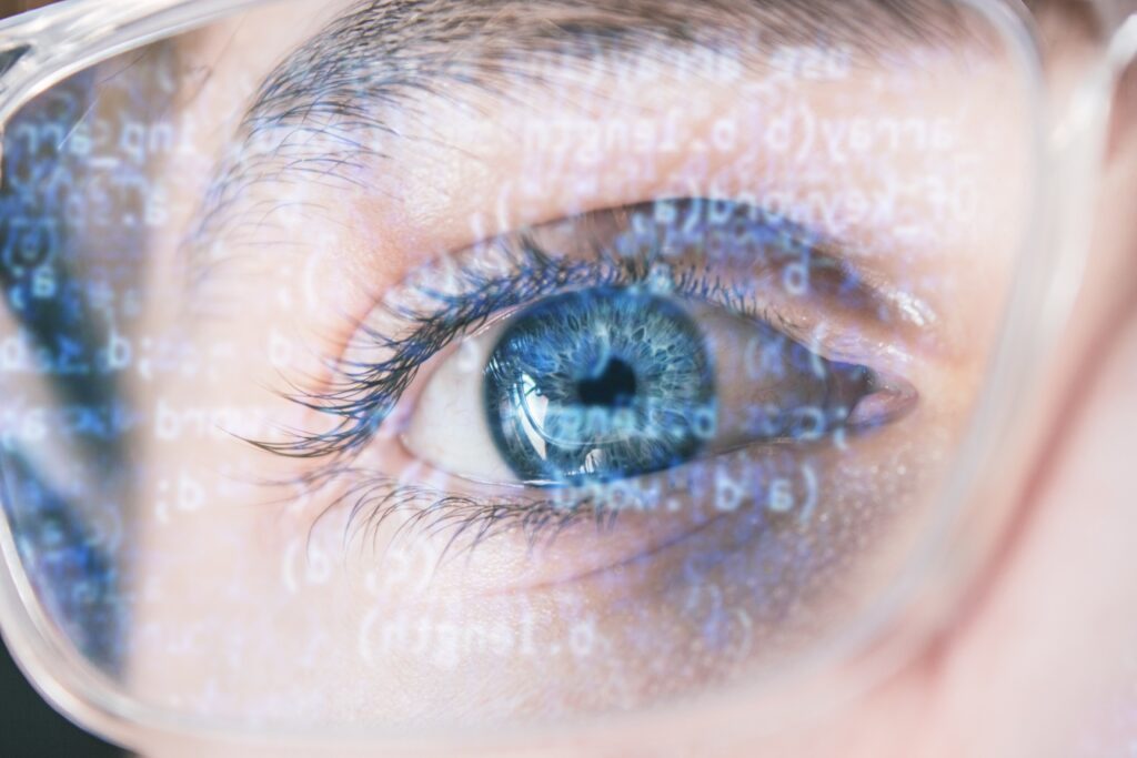 A closeup shot of hacker's blue eye wearing optical glasses with data code reflecting on the glass